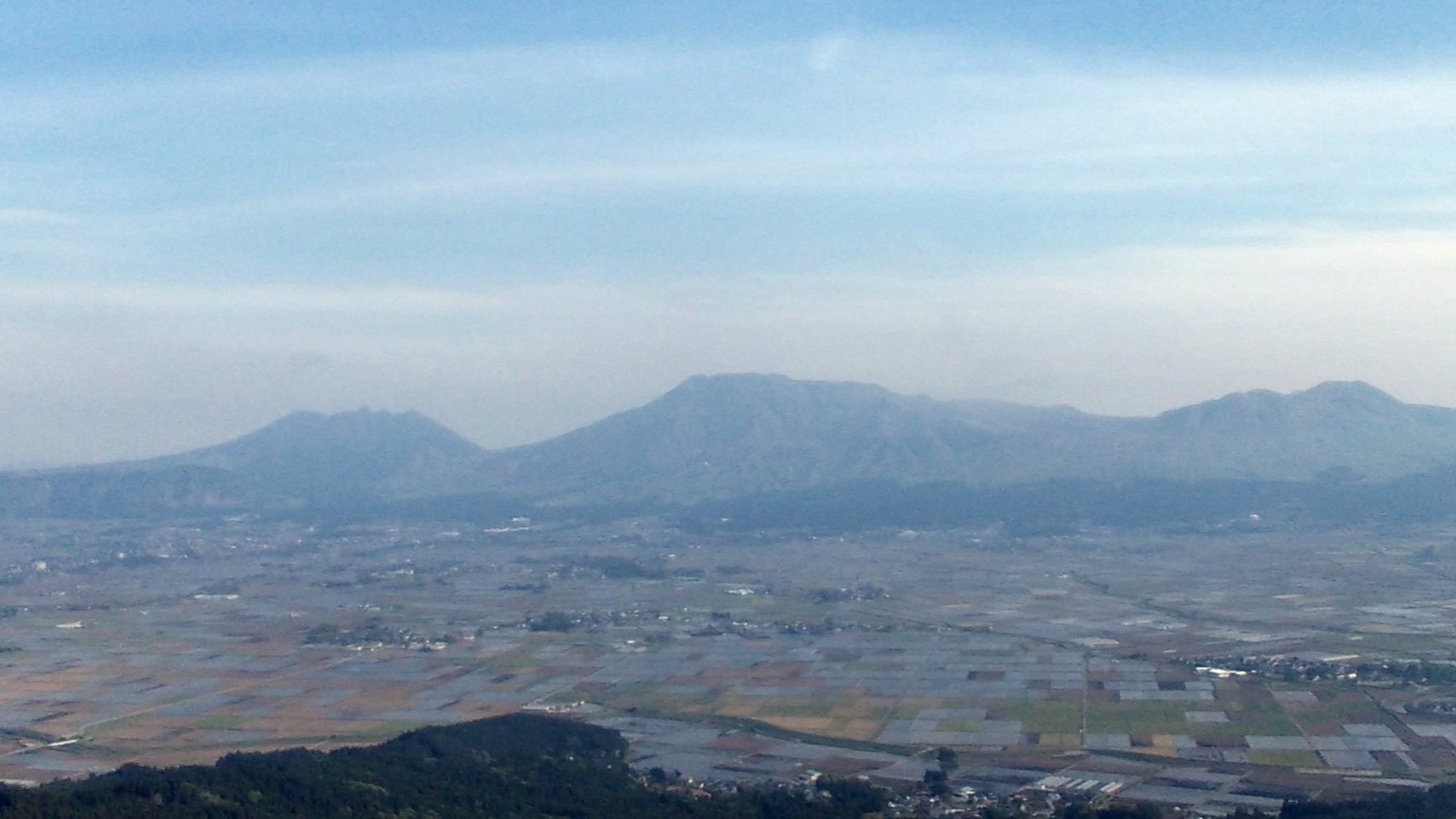 高い場所から見た阿蘇の山並みと、田畑の広がる盆地