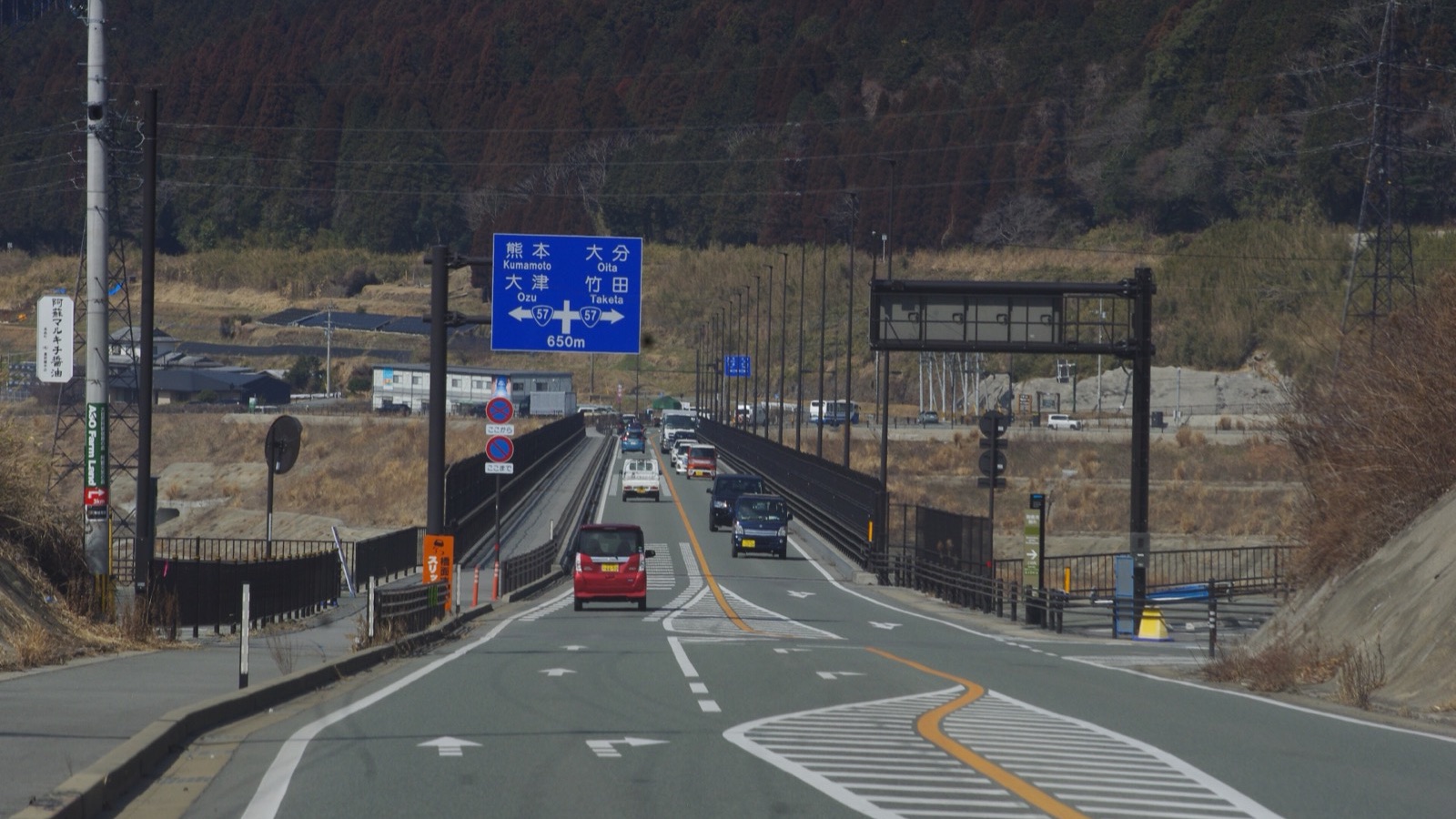 熊本・大分方面の青い案内標識の先へ延びる、車の行き交う橋の道路